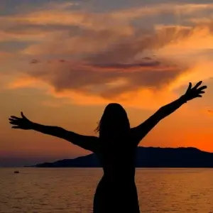 frau steht am meer und hebt die arme.