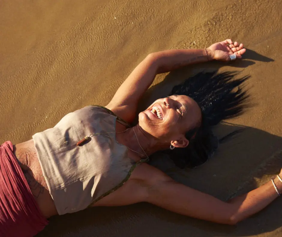 Dunja liegt lachend im Sand und hebt die Hände über den Kopf.
