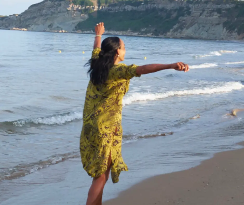 Dunja tanzt am Strand, man sieht im Hintergrund das Meer und Berge