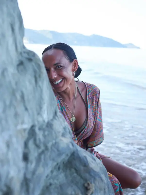 Dunja sitzt am Strand neben einem Felsen und lacht.